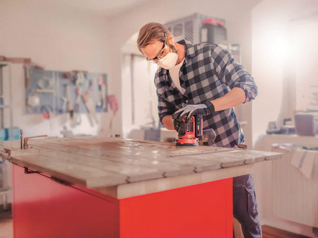 man working with cordless rotating sander in a workshop