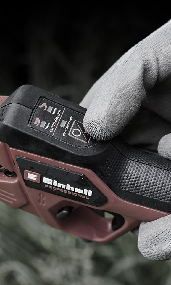 Close-up of a red Einhell cordless device with a gloved hand adjusting its mode.