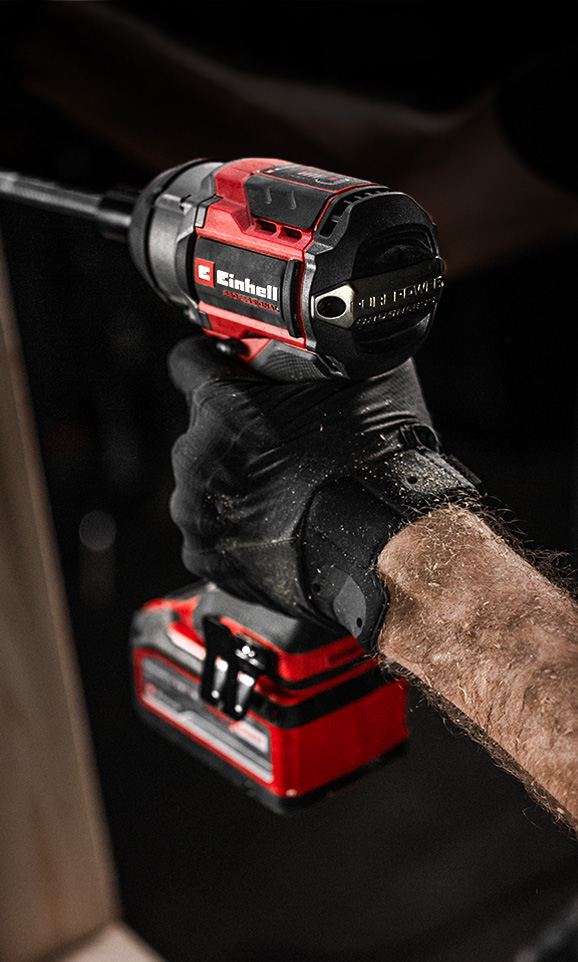 A gloved hand holds a red Einhell cordless impact wrench in use.