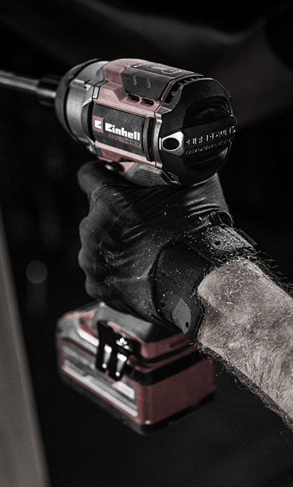 A gloved hand holds a red Einhell cordless impact wrench in use.